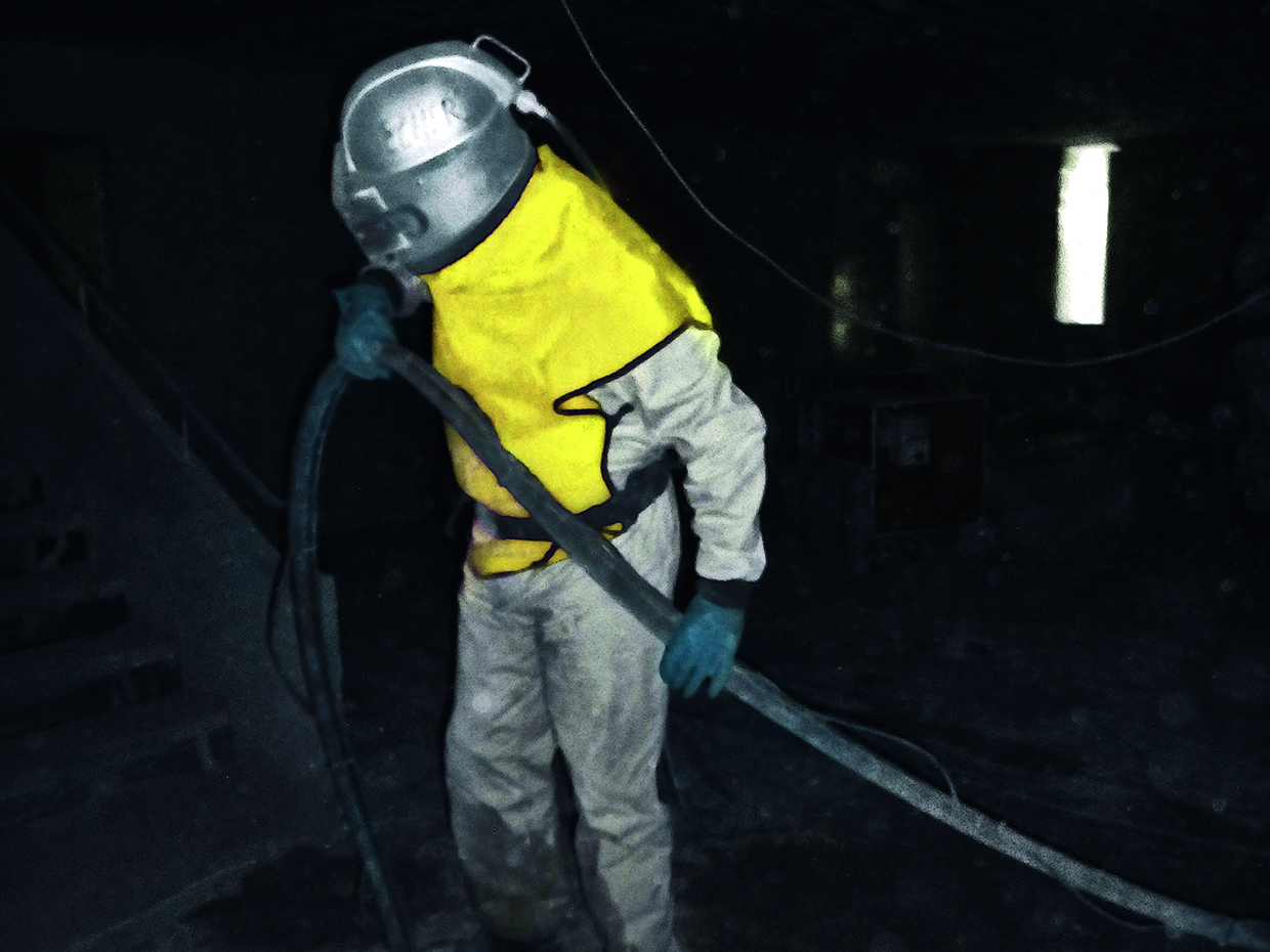  Person wearing protective clothing with fresh-air supply when sandblasting concrete surfaces.